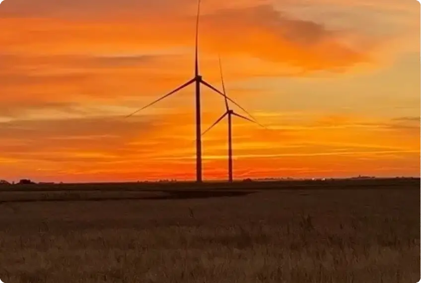 Wind turbines silhouetted against a vibrant sunset sky.